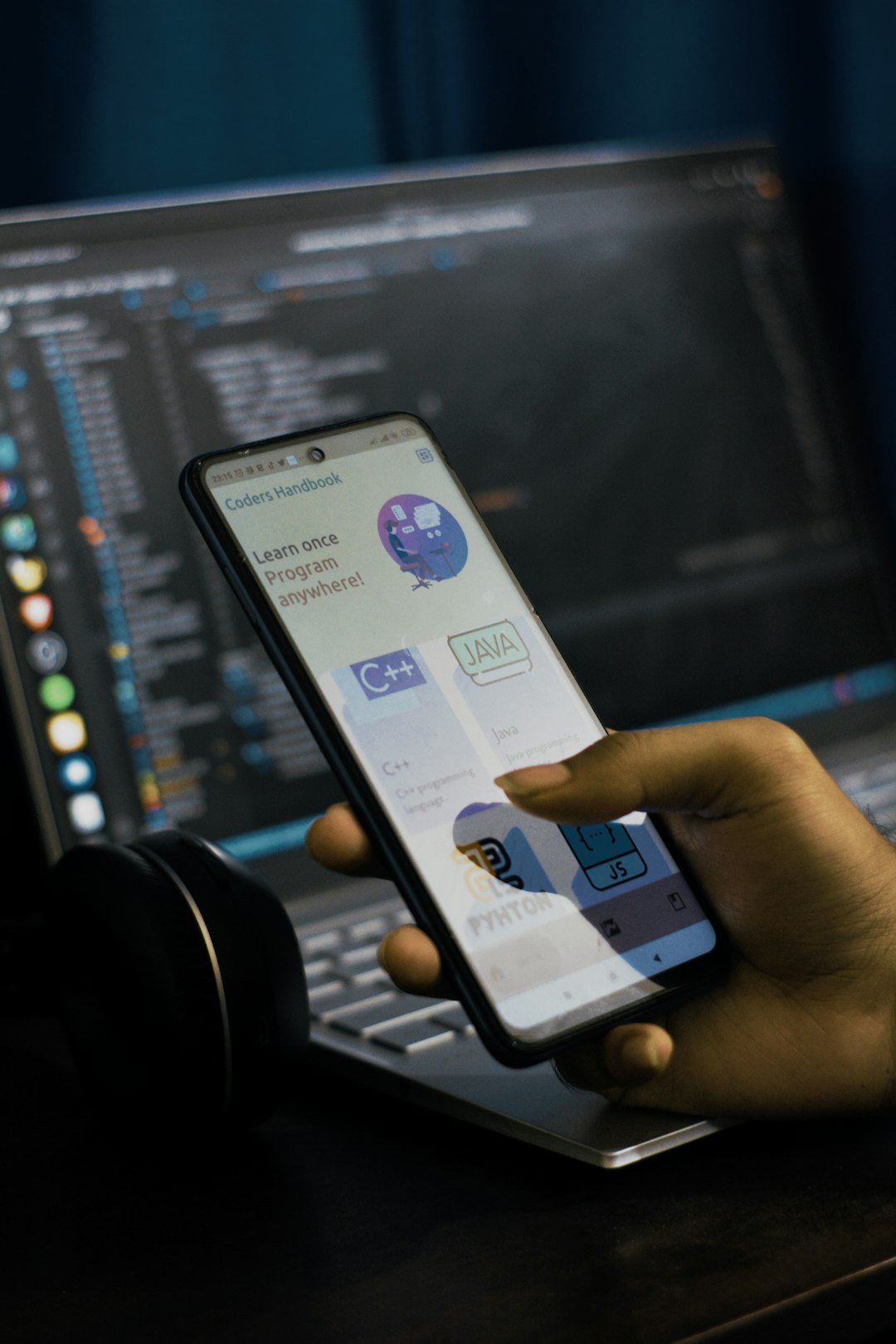 Person holding a smartphone showing an app in front of a laptop