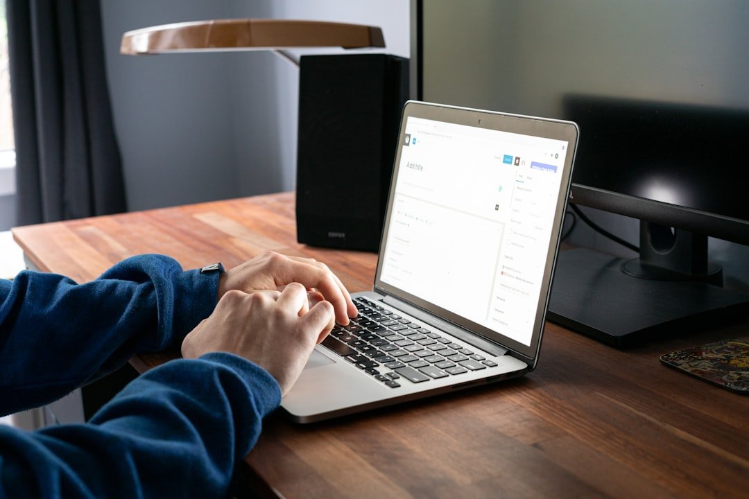 Person using a laptop at a wooden desk, writing content online